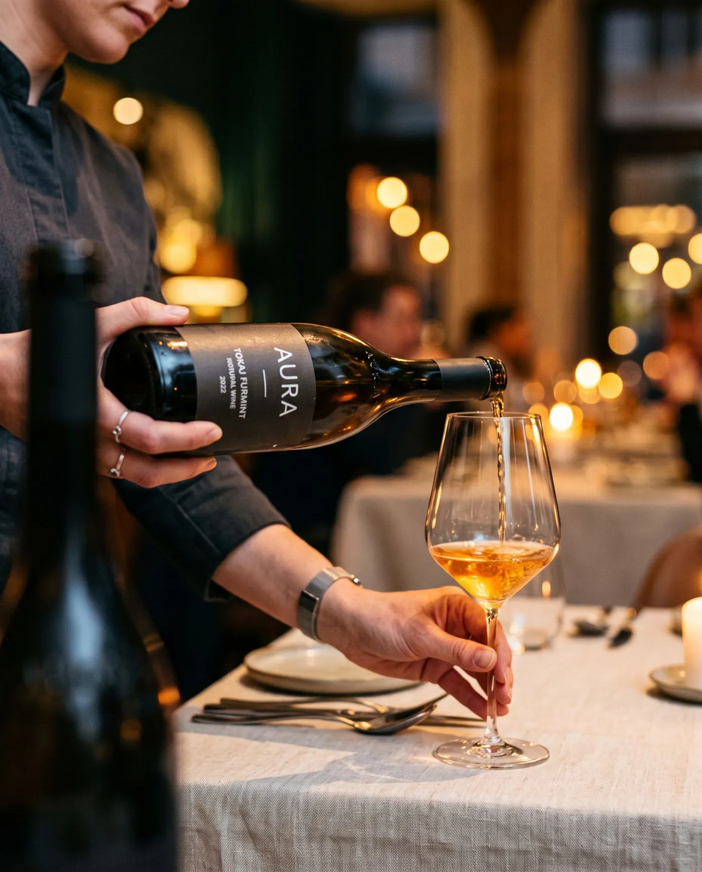 A sommelier natúr bort tölt egy pohárba az étterem félhomályában